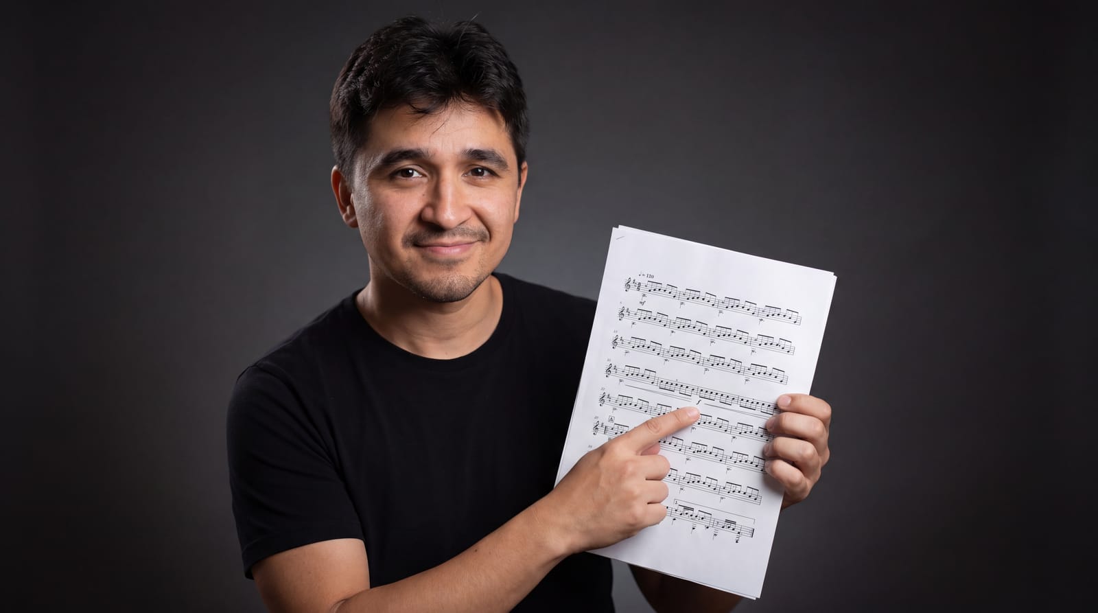 Carlos Jr segurando uma partitura e apontando para um compasso